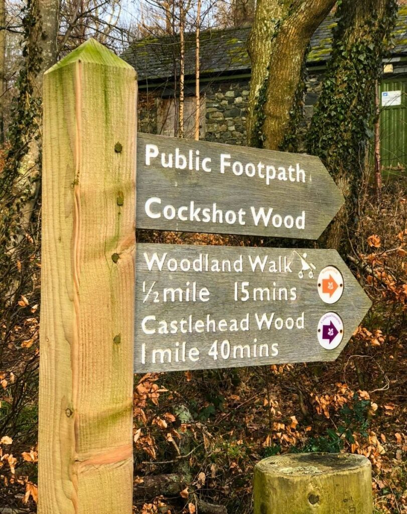 Wooden public footpath fingerpost at the Keswick Derwentwater jetties, pointing the way to Cockshot Wood and the Woodland Walk.