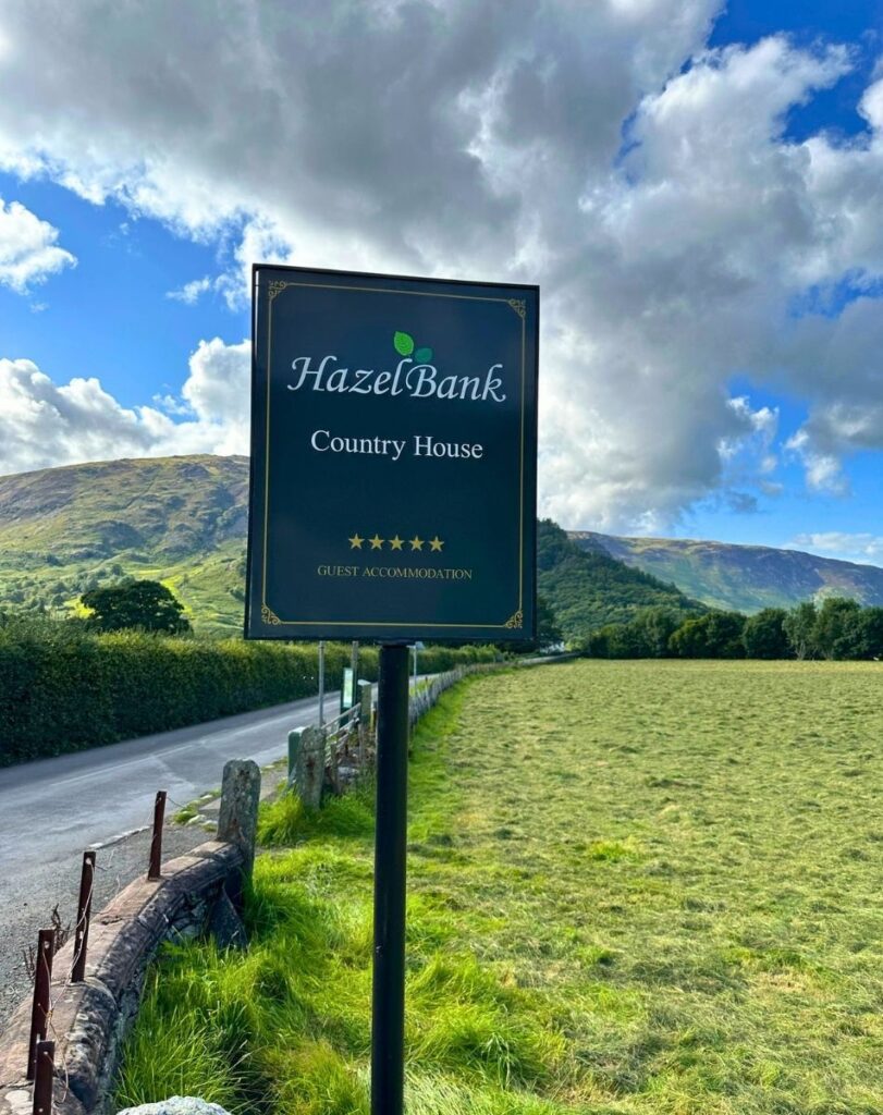 Black and gold five-star sign for Hazel Bank Country House in Rosthwaite, with sweeping green views down the Borrowdale valley towards Keswick.