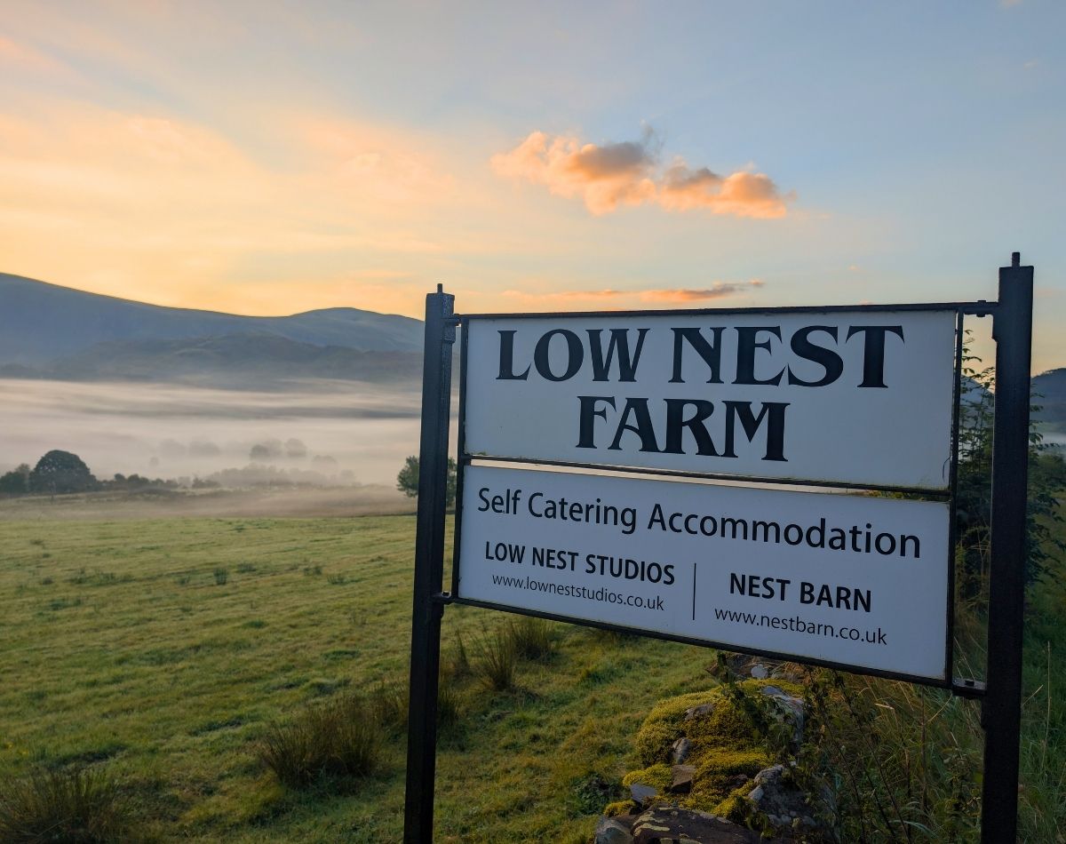 Low Nest Farm self-catering accommodation sign on a stone wall, with a stunning morning cloud inversion and mist rolling through the valley in the background.