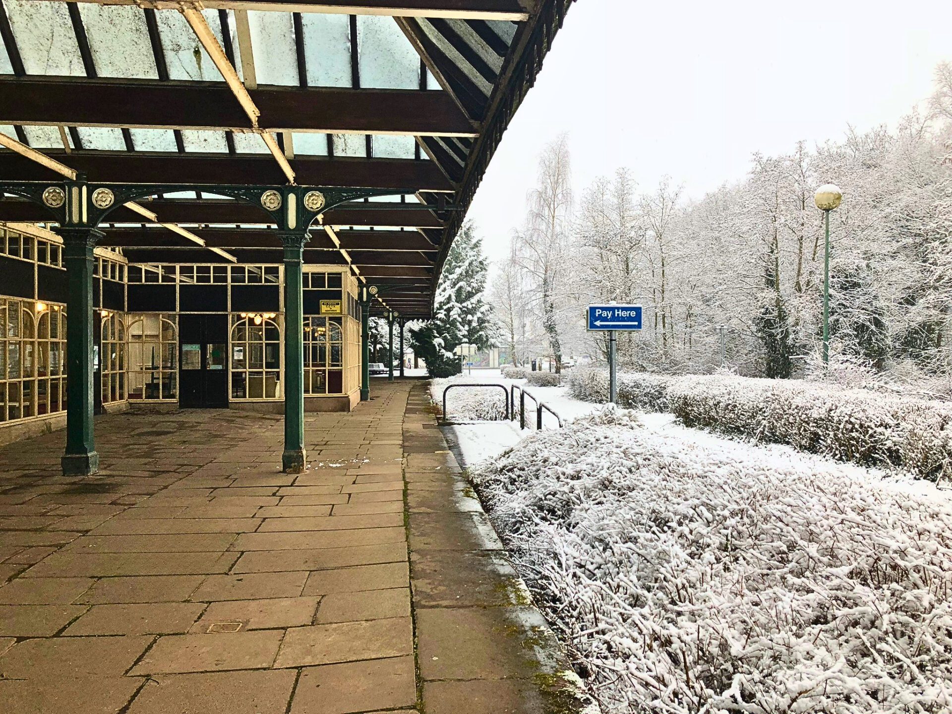 The historic Keswick Railway Station platform featuring original green iron pillars and a Victorian glass canopy, surrounded by fresh winter snow at the start of the Keswick to Threlkeld trail.