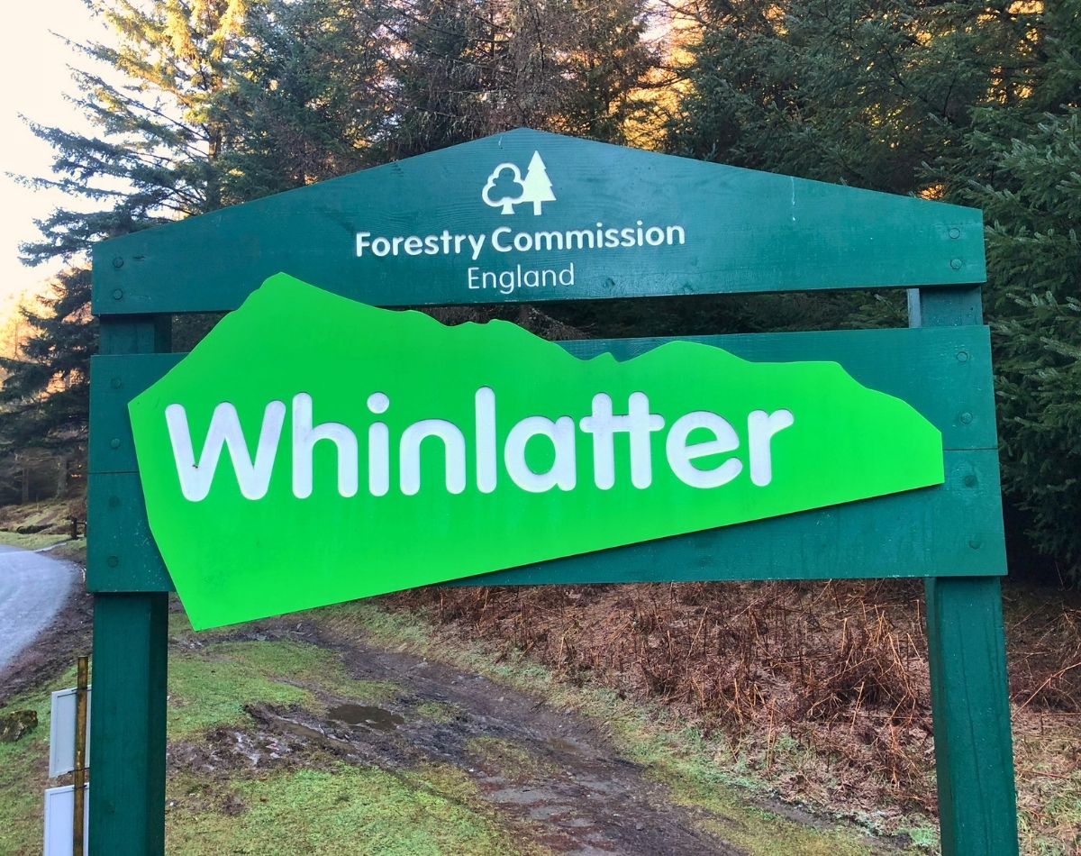 A large wooden Forestry England welcome sign for Whinlatter Forest, located at the visitor centre along the winding B5292 Whinlatter Pass near