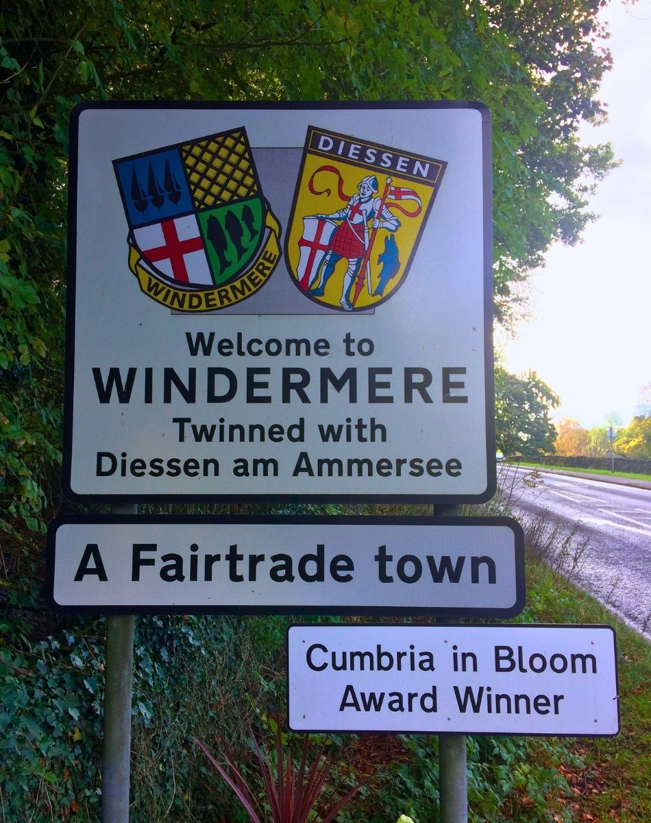 A stone-mounted town welcome sign for Windermere, surrounded by neatly landscaped flower beds and lush green grass.