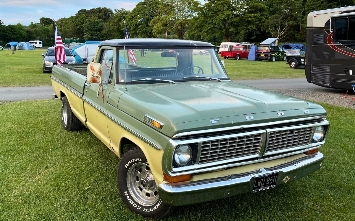 Classic two-tone green and yellow vintage Ford F100 pickup truck displaying American flags at a Lake District car gathering at Pooley Bridge.