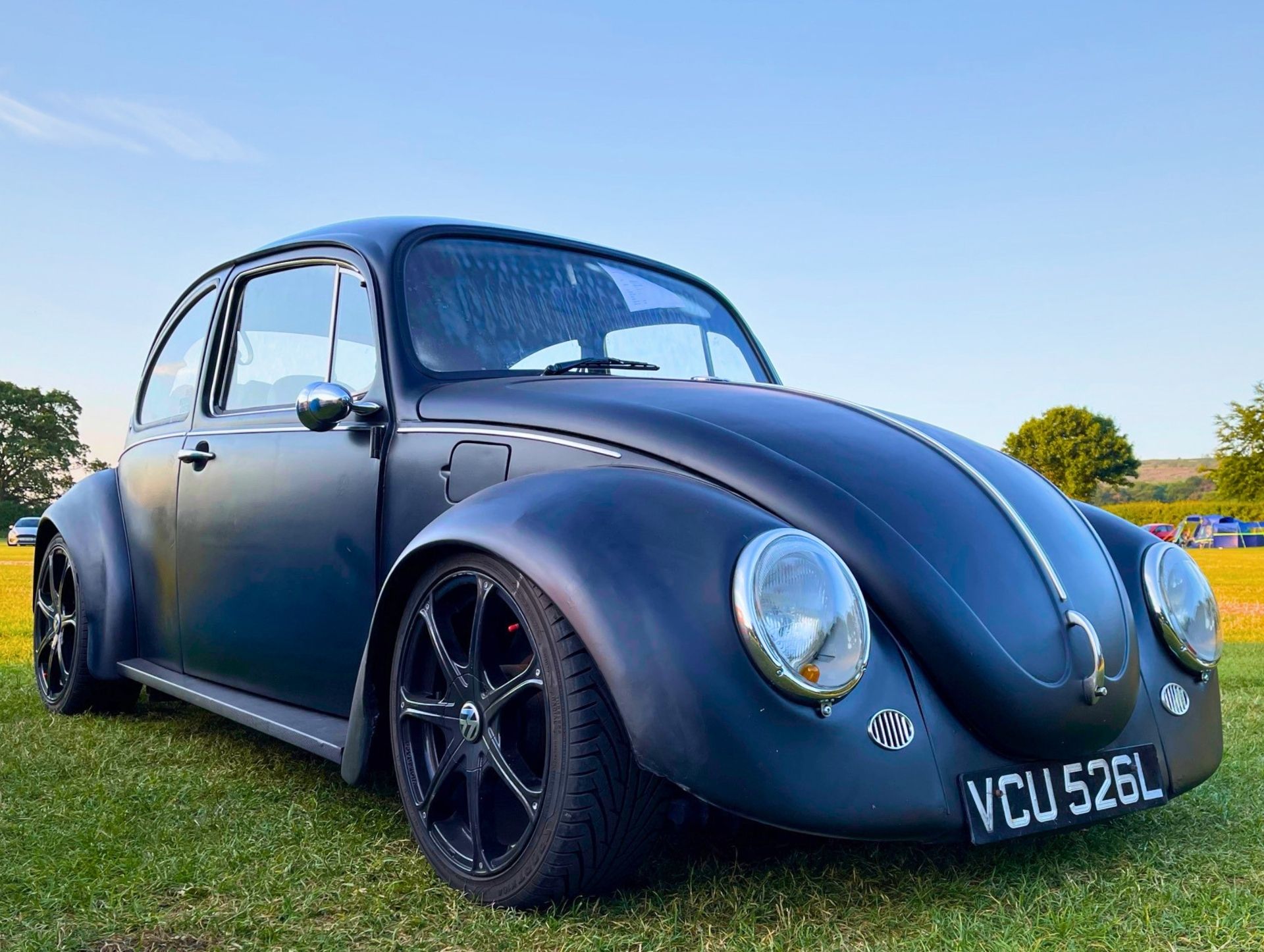 Customised matte black classic VW Beetle lowered on modern black alloy wheels parked on a grassy field at Parkfoot Campsite, Pooley Bridge.