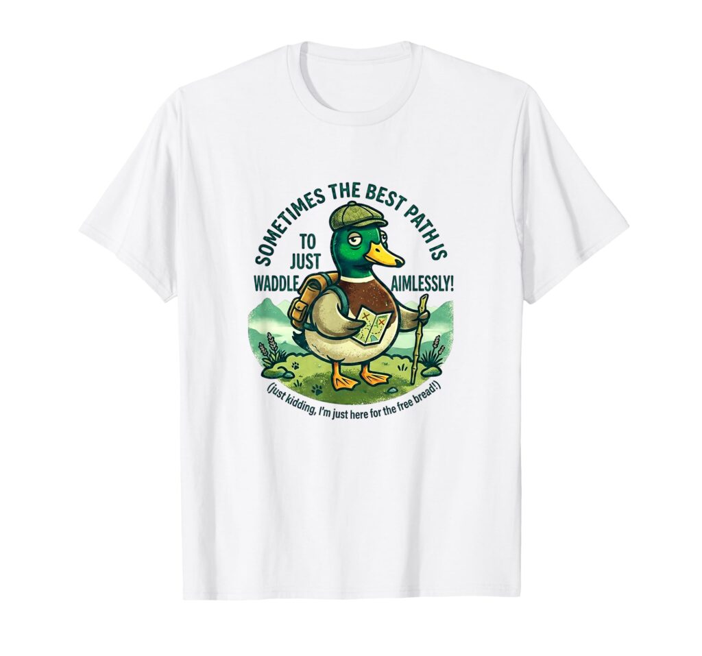 A black t-shirt mockup with a cartoon graphic of a mallard duck wearing a beanie and hiking backpack, with curved text that reads "WADDLE AIMLESSLY AROUND THE LAKE DISTRICT."