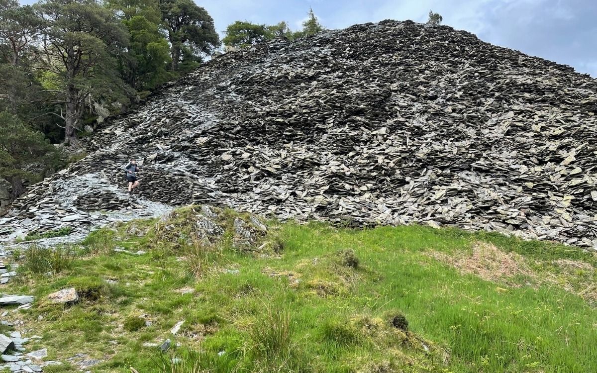 Steep zigzag footpath winding through loose grey slate quarry scree on the final ascent to the summit of Castle Crag in Borrowdale.