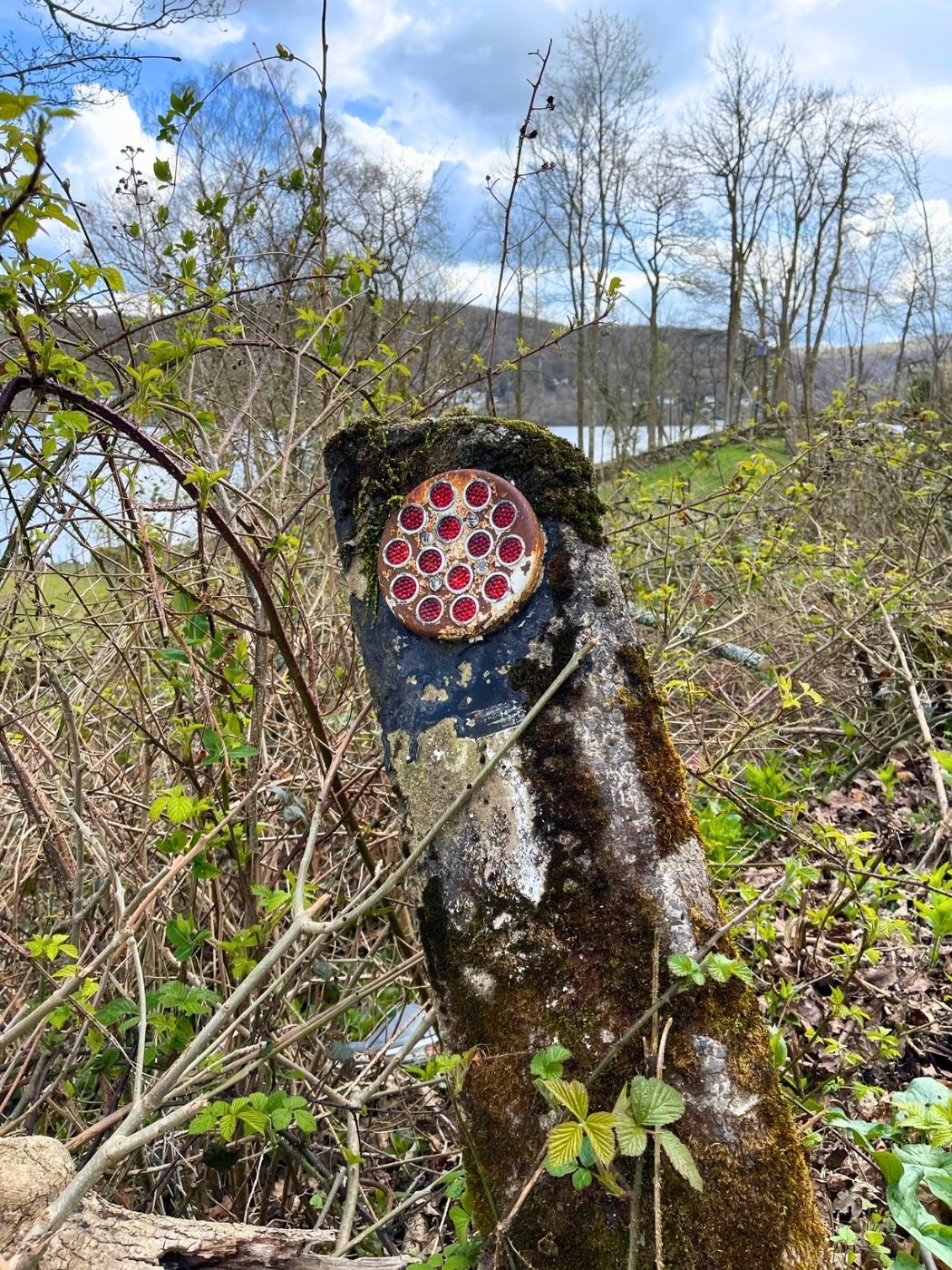 An old, weathered traditional cast iron road sign pointing the way, with the expansive waters of Windermere and the surrounding fells visible in the background.