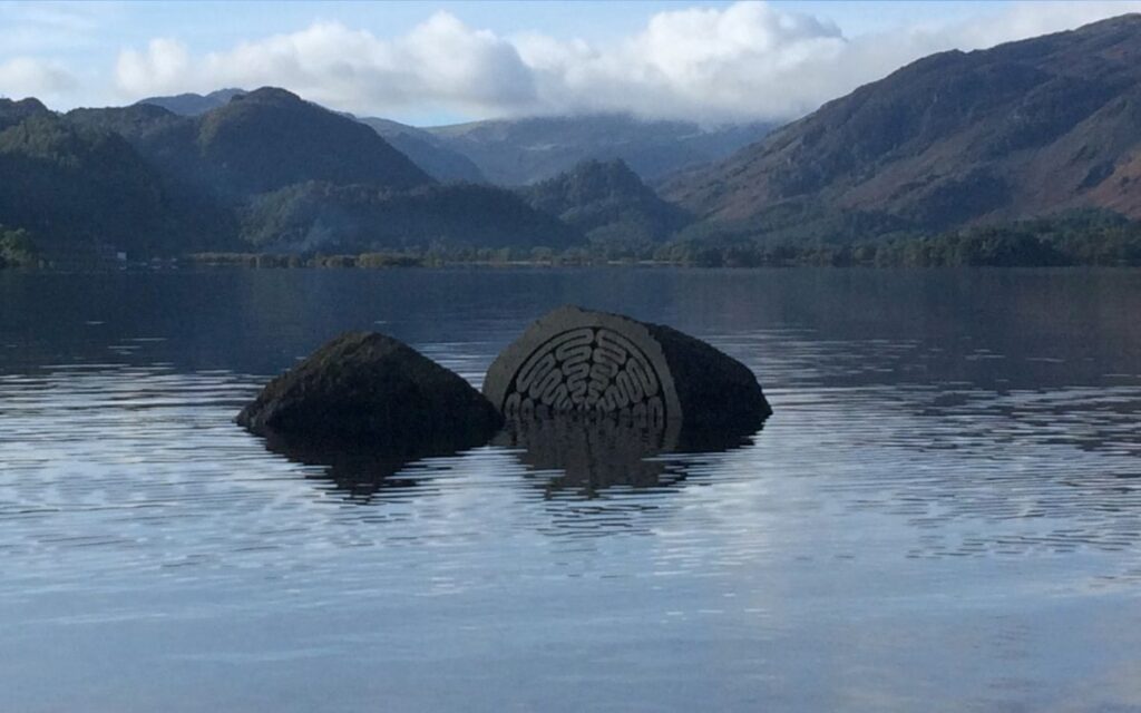 Peter Randall-Page's carved Centenary Stone partially submerged at Calfclose Bay on Derwentwater, looking south towards Castle Crag and Borrowdale.