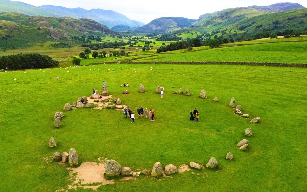 High elevated view of visitors exploring Castlerigg Stone Circle surrounded by the sweeping emerald valley and dramatic northern Lake District peaks.