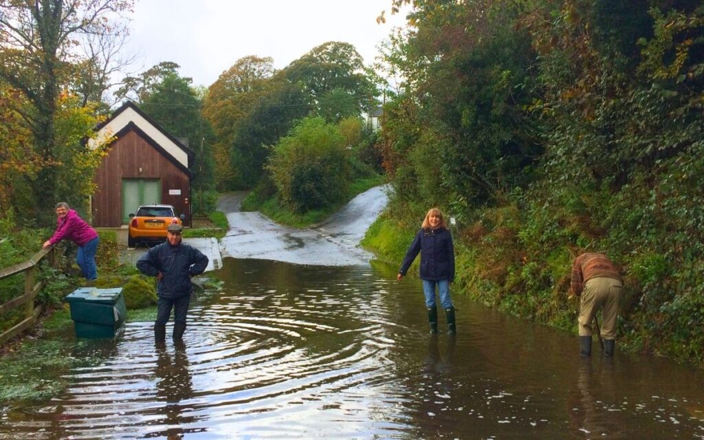 Deep flood water covering the road in Bassenthwaite village with local residents in wellies inspecting the blockage.