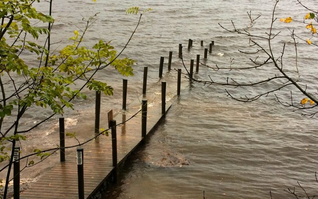 Slender wooden boardwalk of the old Ashness Jetty disappearing beneath the grey, swollen surface of Derwent Water during flood conditions.